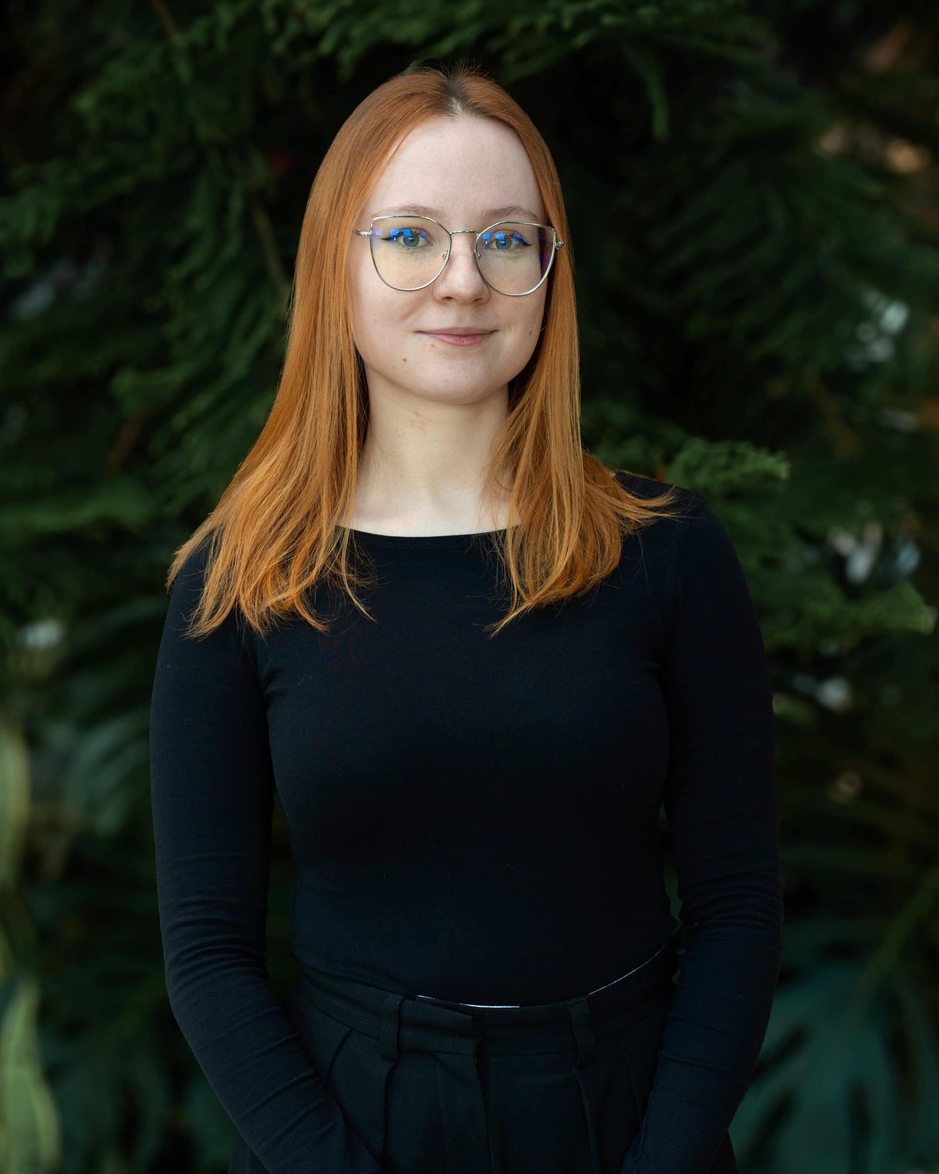 Professional headshot of a woman wearing a black shirt, standing in front of a tree.