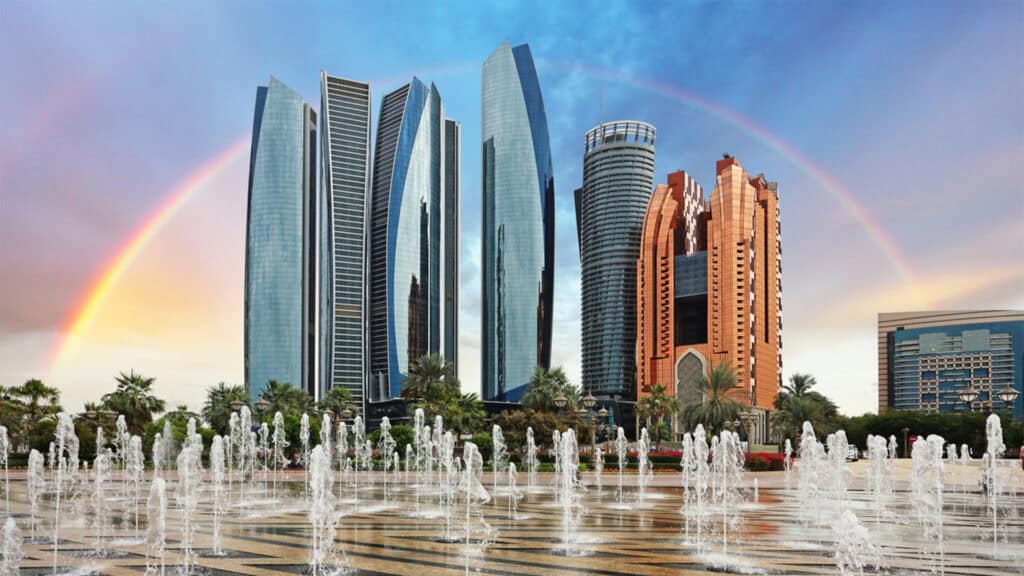 Modern Dubai skyline with fountains and a vibrant rainbow in the background.