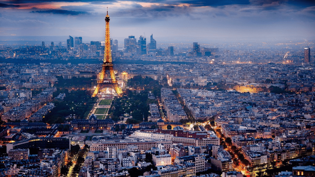 Eiffel Tower illuminated over Paris cityscape at dusk, showcasing iconic landmarks and vibrant urban environment.