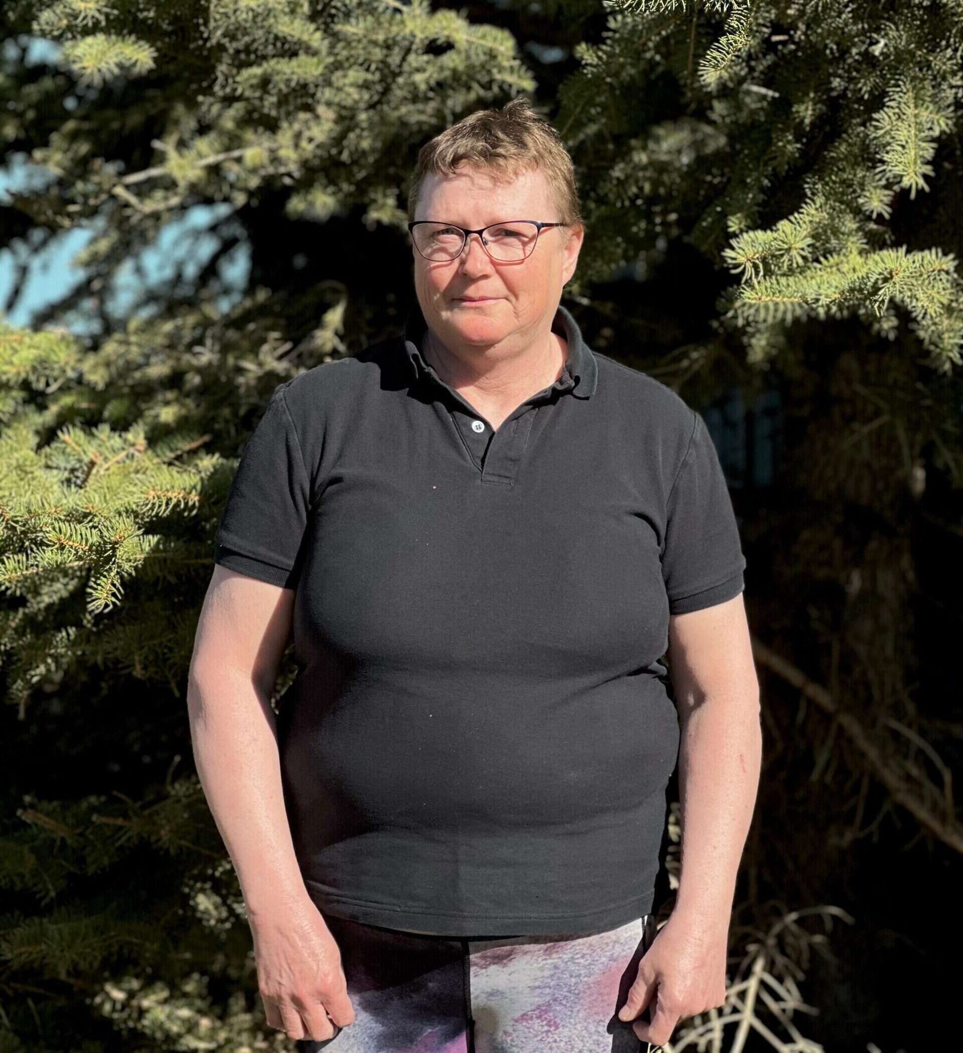 Professional headshot of a woman in a black shirt, standing in front of a tree.