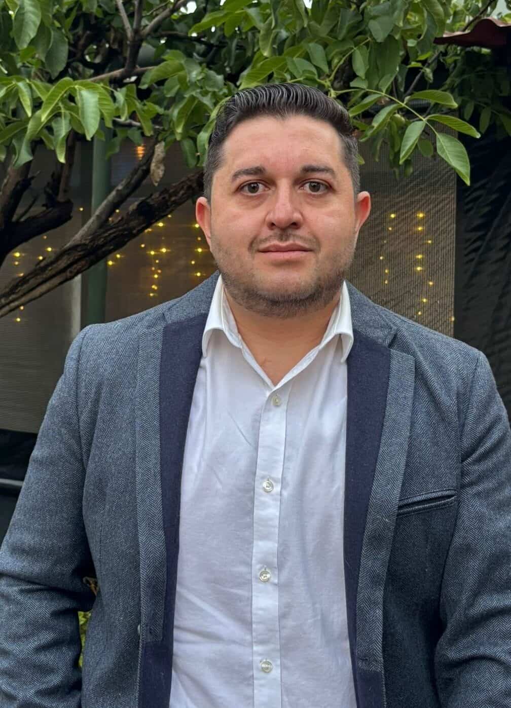 Richmond man in blazer sitting outdoors with lush greenery background.