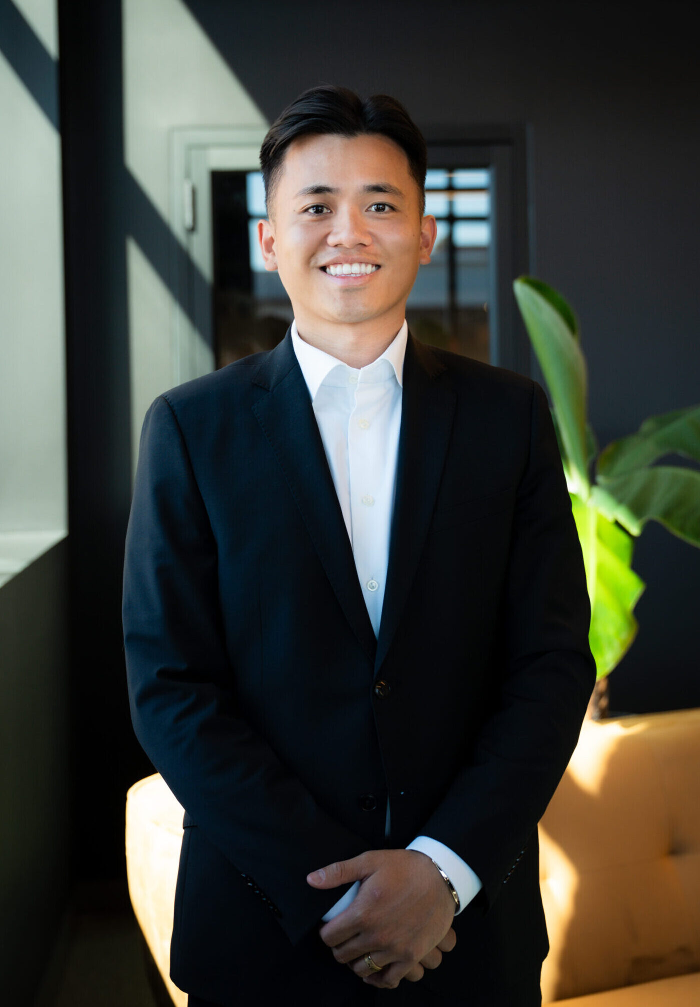 Confident businessman in formal suit smiling indoors at modern office with plants.